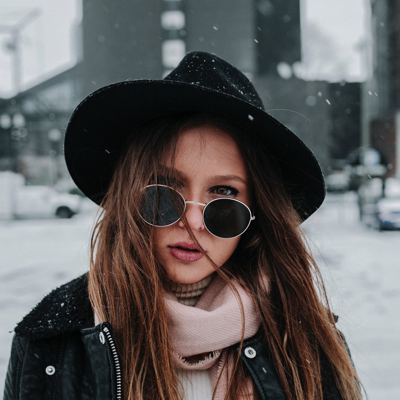Woman wearing a black hat and sunglasses in a snowy setting.